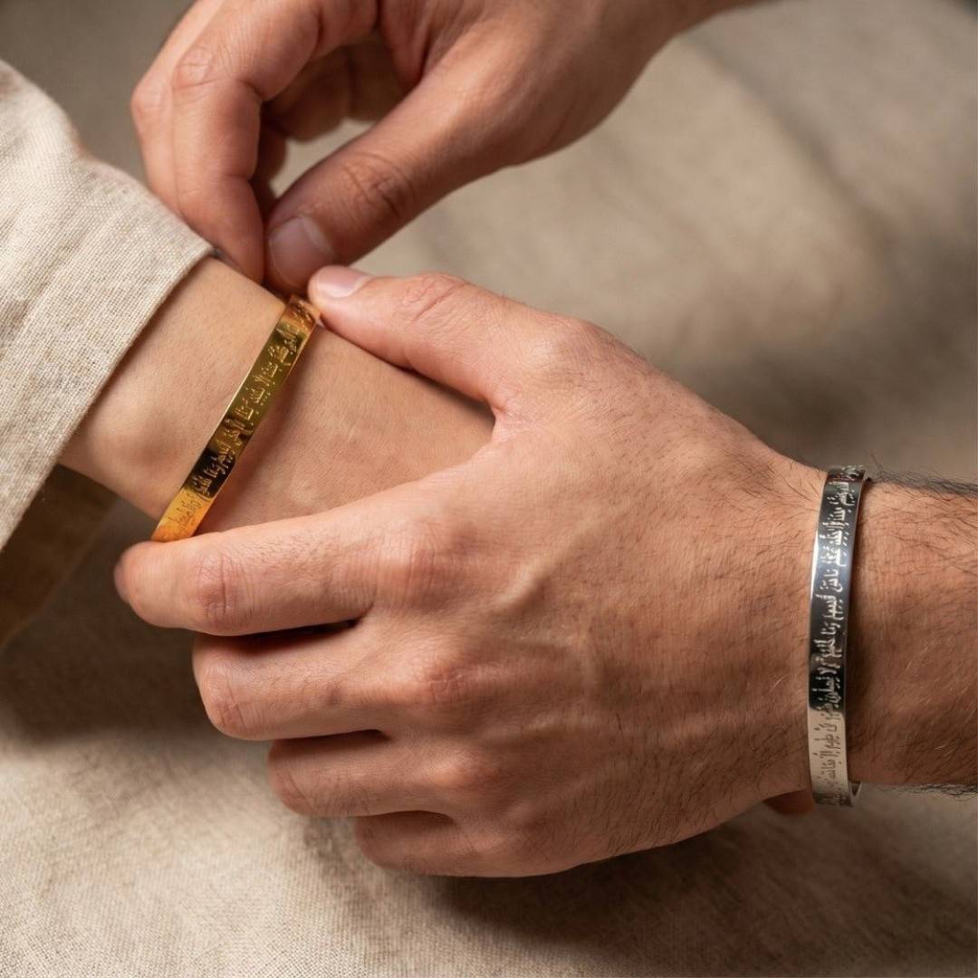 A close-up lifestyle shot of a person's hands adjusting a gold-toned metal cuff bracelet on their wrist, with another silver-toned cuff bracelet visible on the other wrist, set against a neutral beige background.