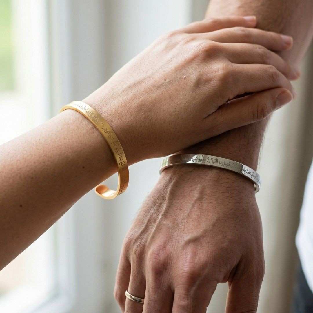 A close-up lifestyle shot of two engraved cuff bracelets on wrists, one gold-toned and one silver-toned, worn by a couple with one hand resting on the other's forearm.