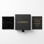 Luxorai jewelry packaging set on a white background, featuring a black velvet pouch with gold lettering, a central black presentation box with gold 'LUXORAI' text, and a black card with gold text.