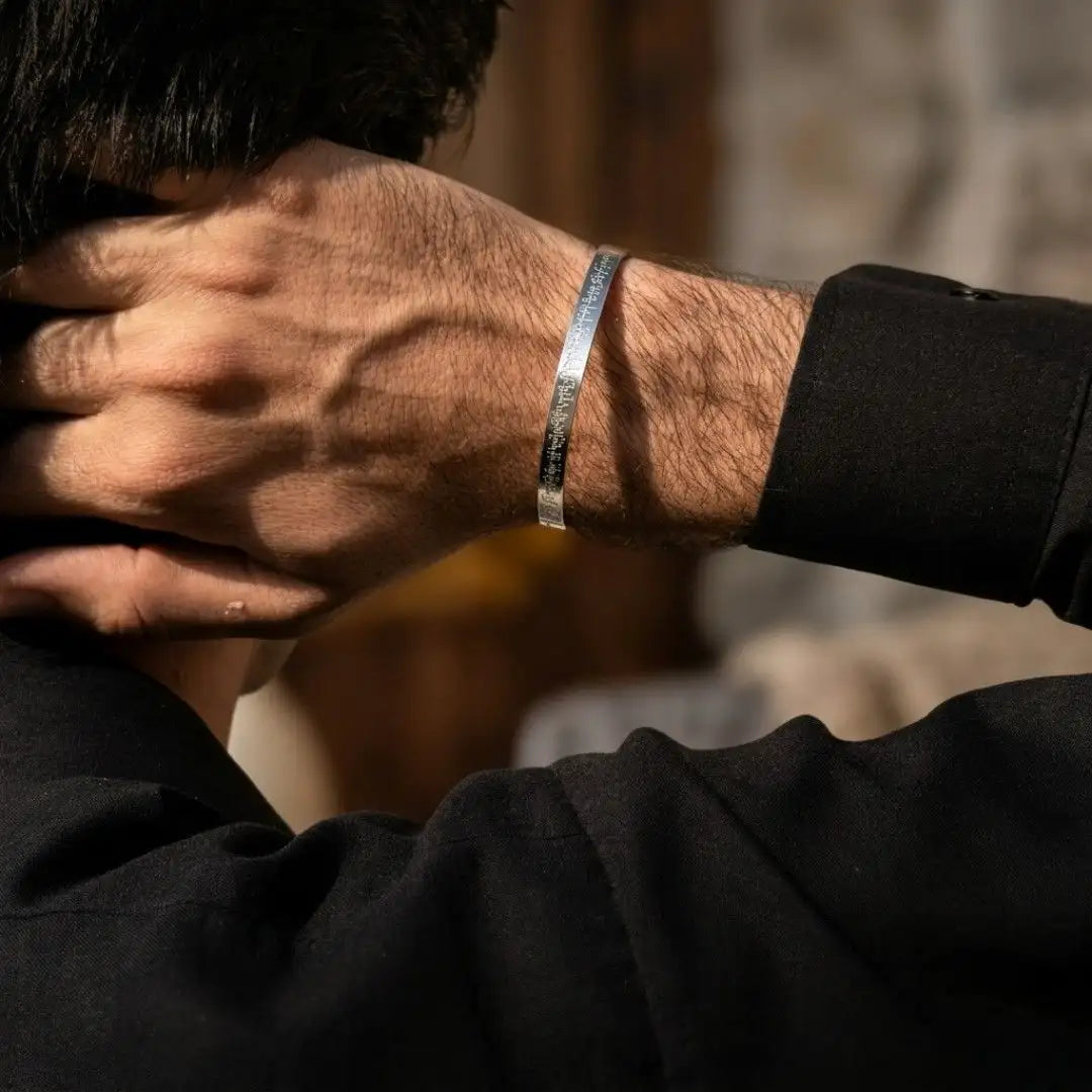 A close-up lifestyle shot of a man's hand and wrist wearing a slim, engraved silver metal cuff bracelet.